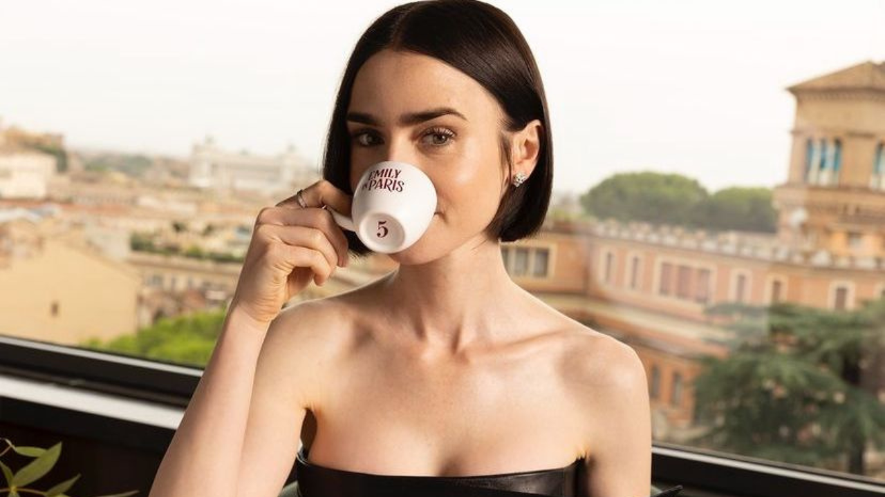 Emily tomando una taza de café en el que se ve que lleva como numero 5