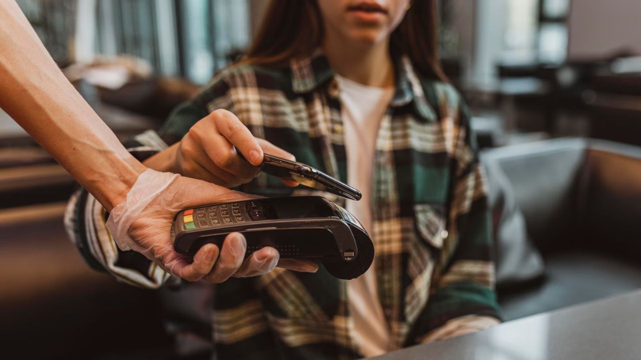 Mujer joven pagando algo en una terminal bancaria durante la cuesta de enero 