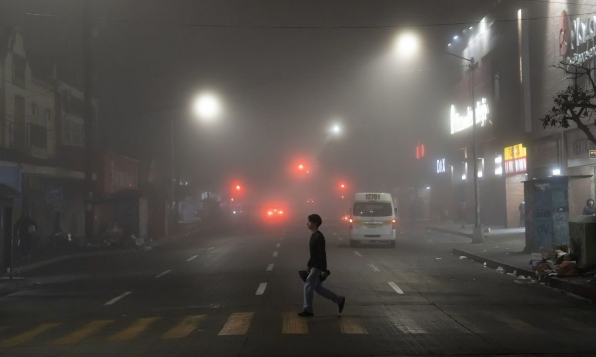 Un peatón cruzando una avenida ante la presencia de un banco de neblina ante la alerta por frío.