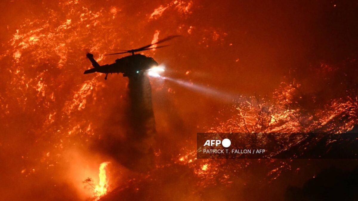 Un helicóptero de extinción de incendios arroja agua mientras el incendio de Palisades, Los Ángeles, crece.