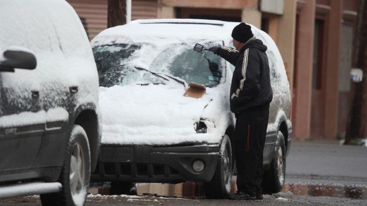 Un señor quitando la capa de hielo de la superficie de su vehículo por el paso de la Tormenta invernal en México.