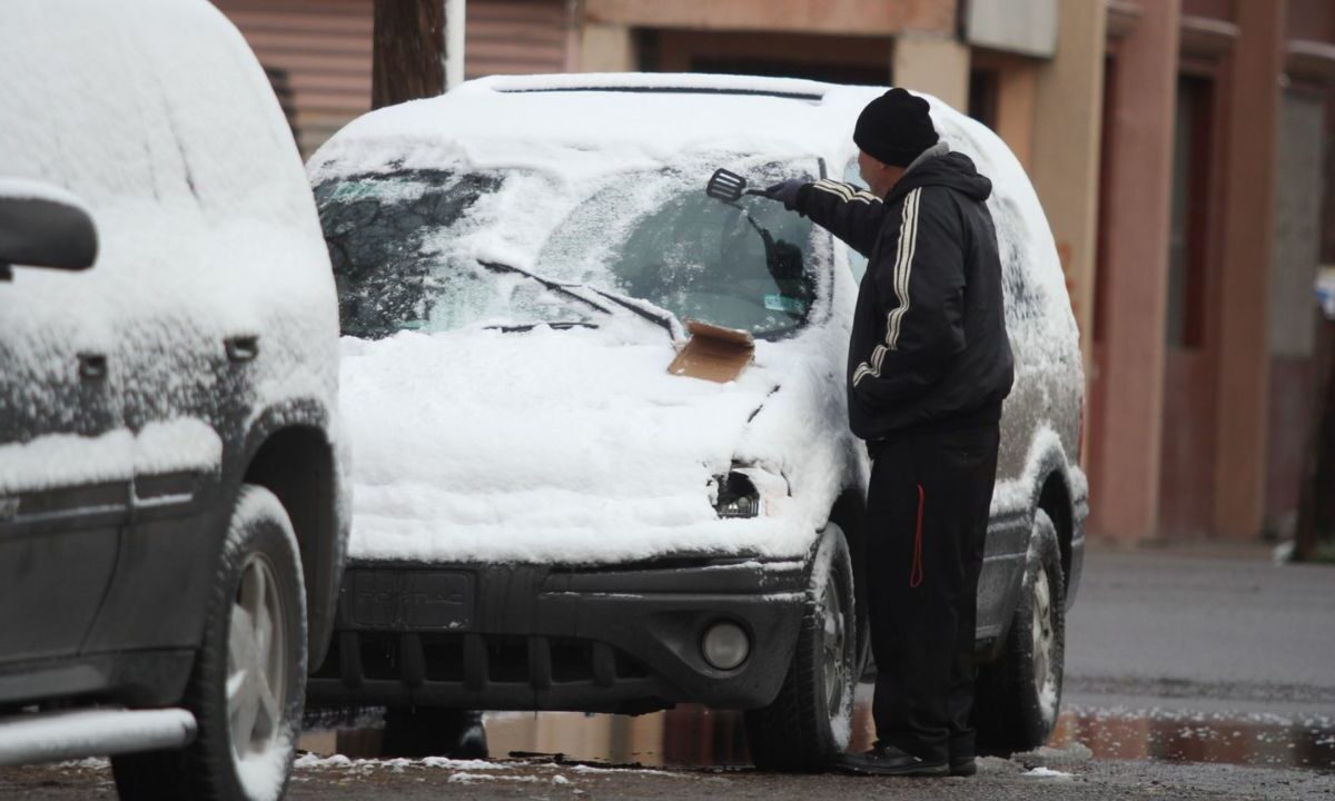 Un señor quitando la capa de hielo de la superficie de su vehículo por el paso de la Tormenta invernal en México.