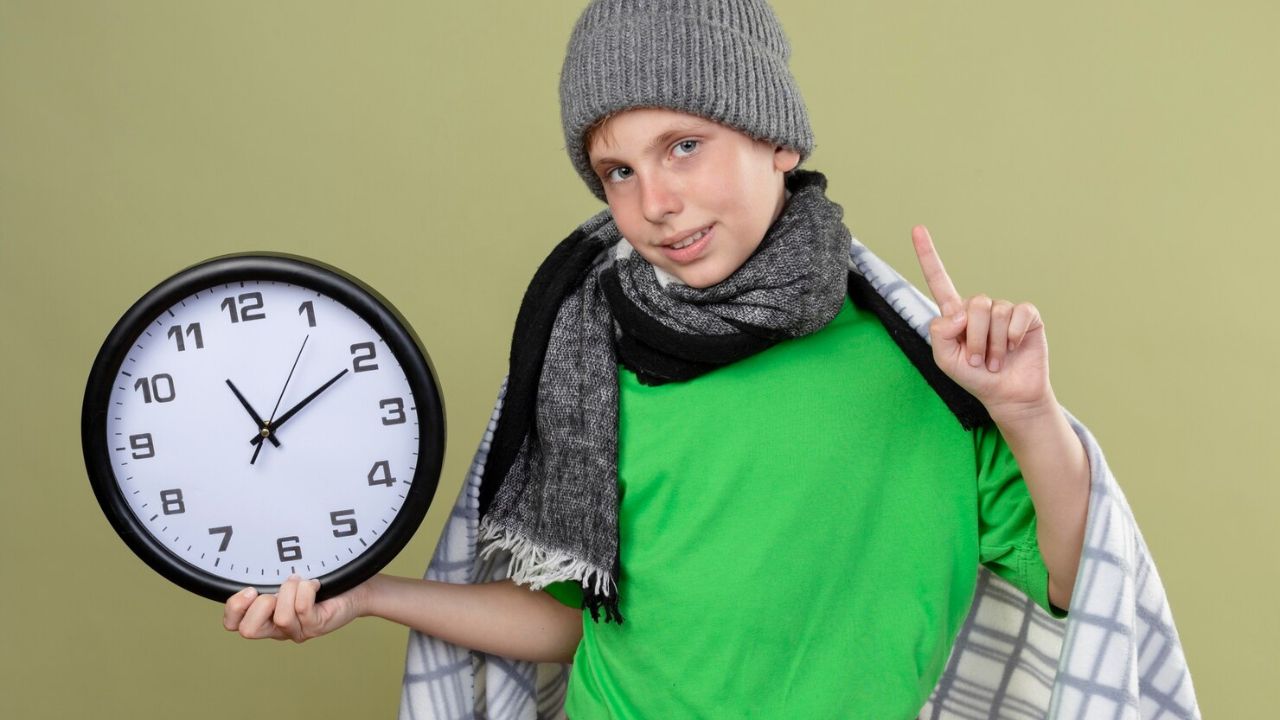 Niño sosteniendo un reloj de pared que indica el horario de invierno 