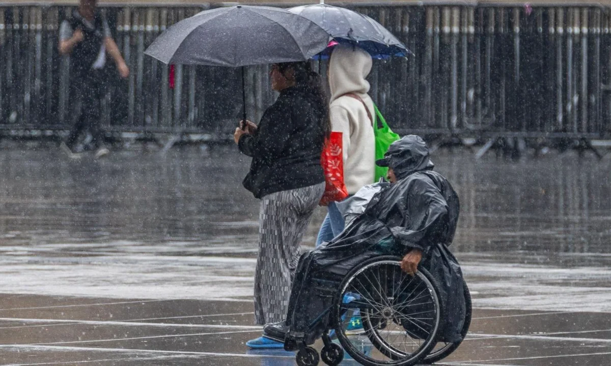 Personas cubriéndose con paraguas o impermeables tras llovizna ligera en el Zócalo de la Ciudad de México.