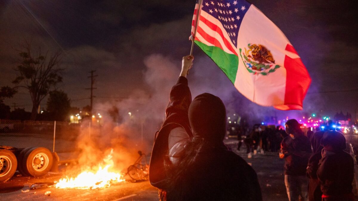 Aunque hay operativos, las manifestaciones siguen. Fernando Delgado, joven hispano con una bandera mexicana frente a un vehículo calcinado, lo dice claro: “Somos trabajadores, no criminales.”